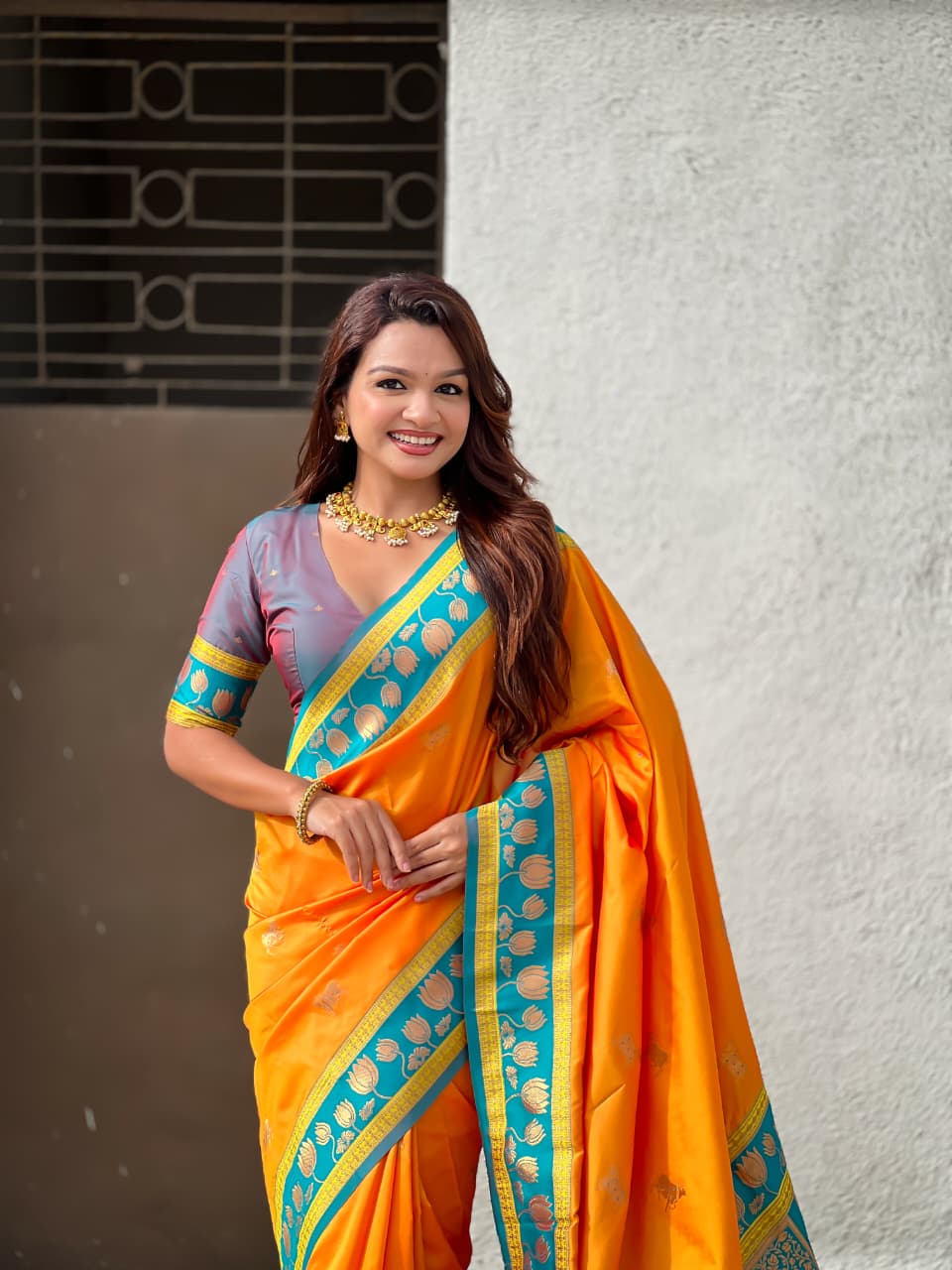 Festive wear orange Paithani silk saree with teal border, lotus artwork and luxurious ethnic styling.